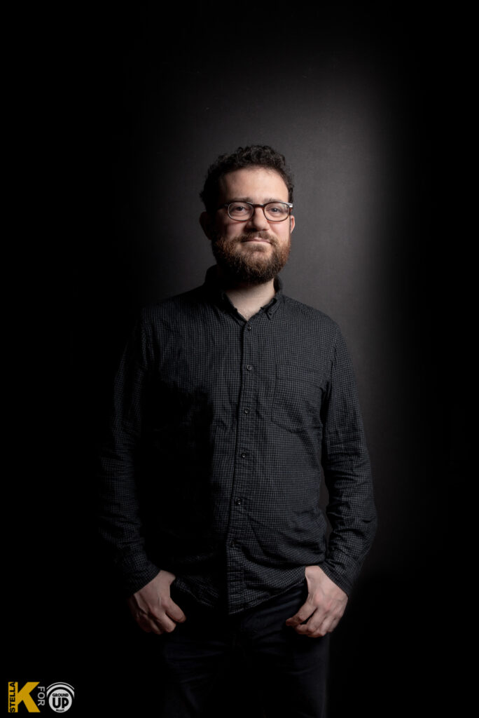 a man with glasses standing in a dark room